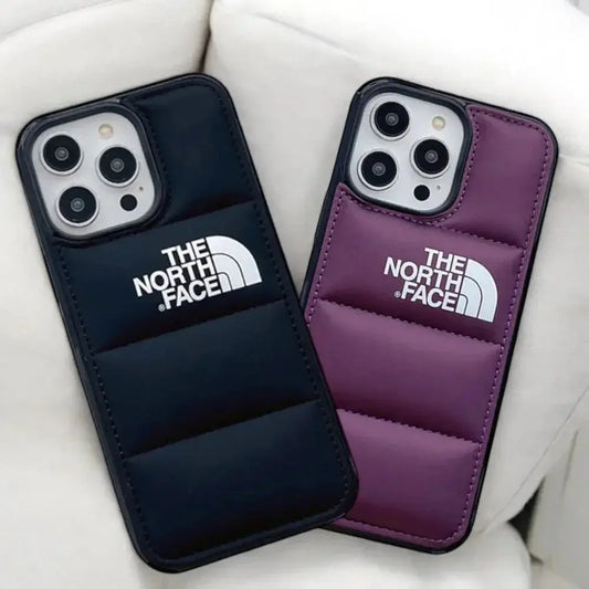 Two The North Face padded phone cases, one black and one purple, on a white couch