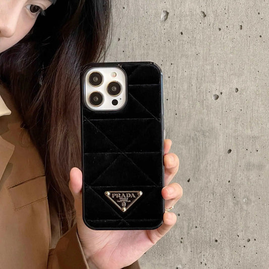 Hand holding iPhone with black velvet Prada phone case against concrete wall