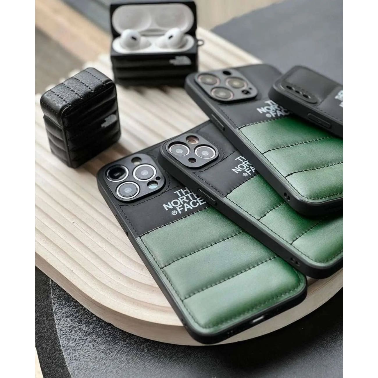 Green and black padded iPhone cases with The North Face branding on a wooden tray