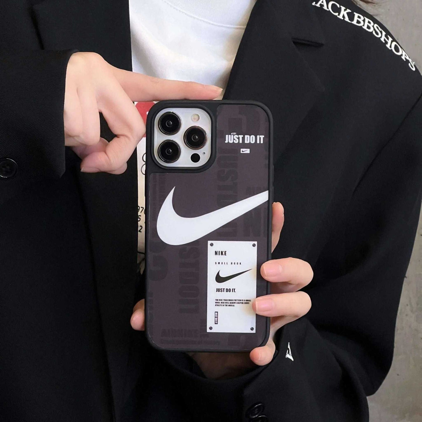 Hand holding iPhone with black Nike sports case featuring white swoosh and 'Just Do It' slogan.