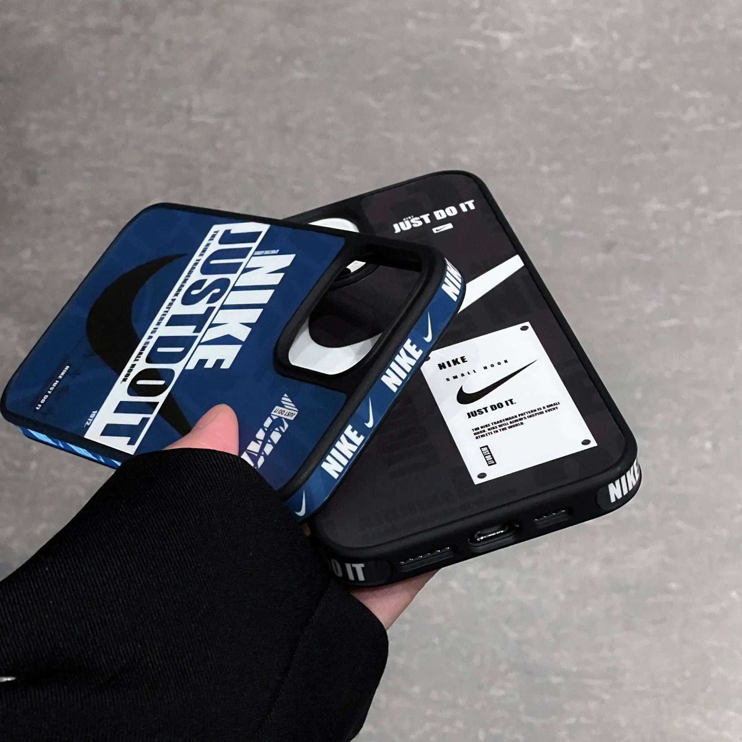 Hand holding two Nike sport iPhone cases with Just Do It slogan, blue and black design.