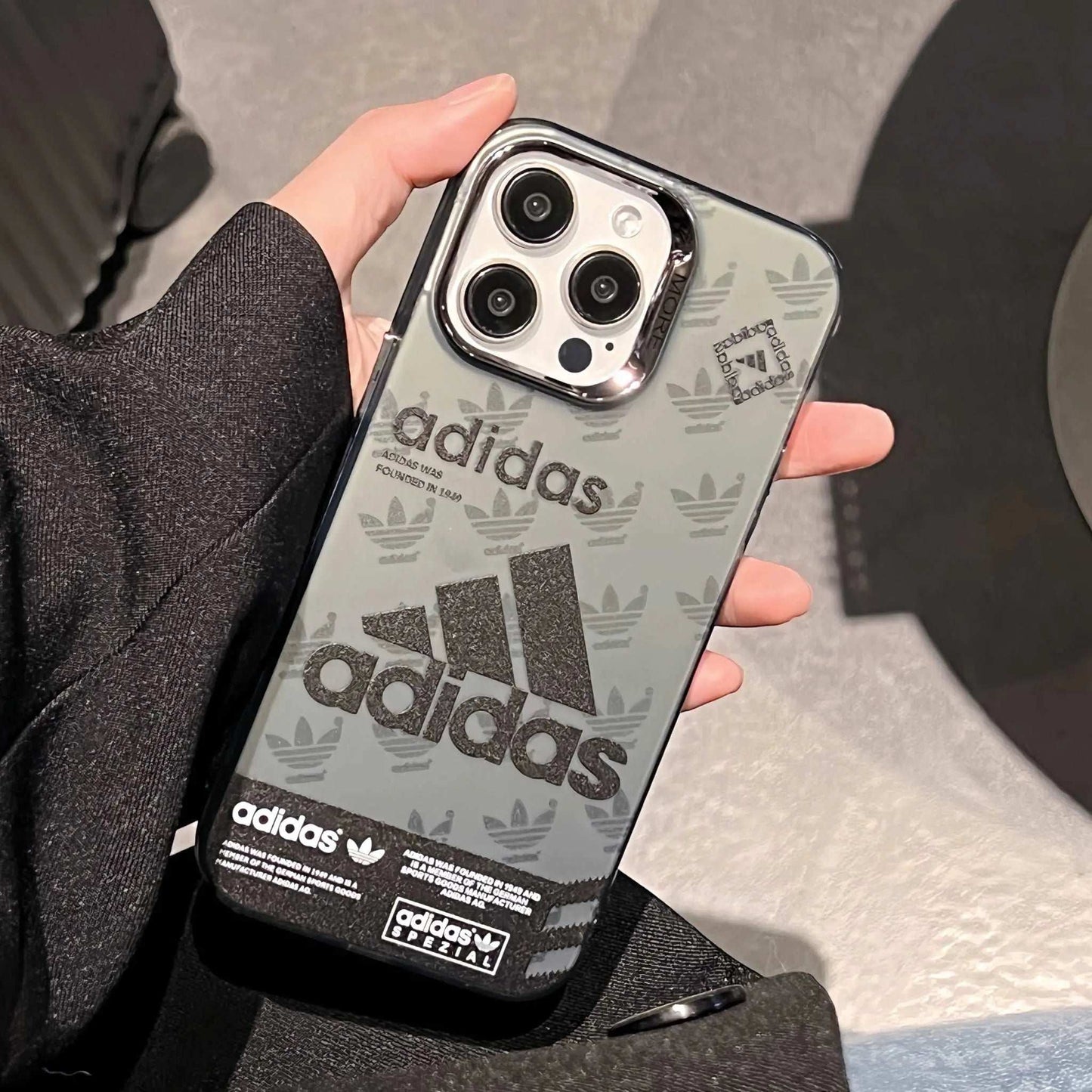 Adidas logo sport iPhone case in hand, clear back, black Trefoil and branding.