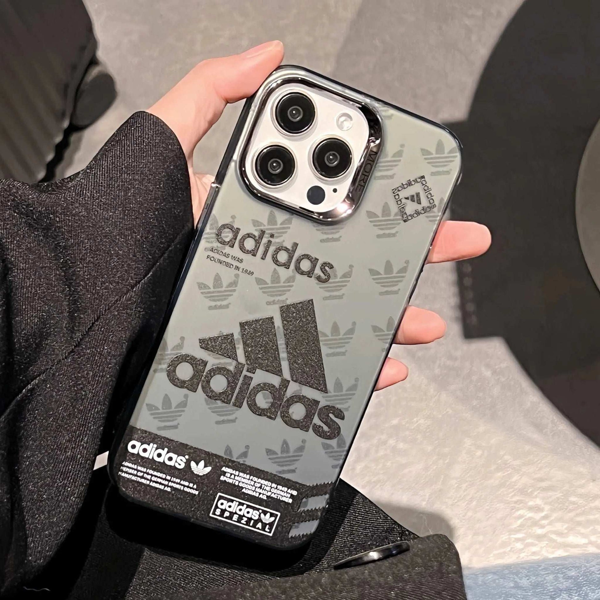 Adidas logo sport iPhone case in hand, clear back, black Trefoil and branding.