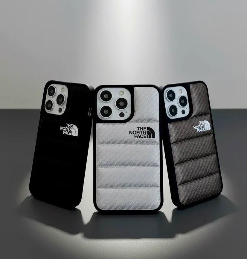 Three The North Face branded iPhone cases in black, white, and gray with quilted texture on a table.