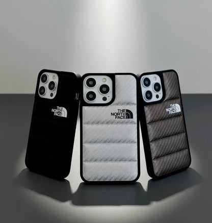 Three The North Face branded iPhone cases in black, white, and gray with quilted texture on a table.