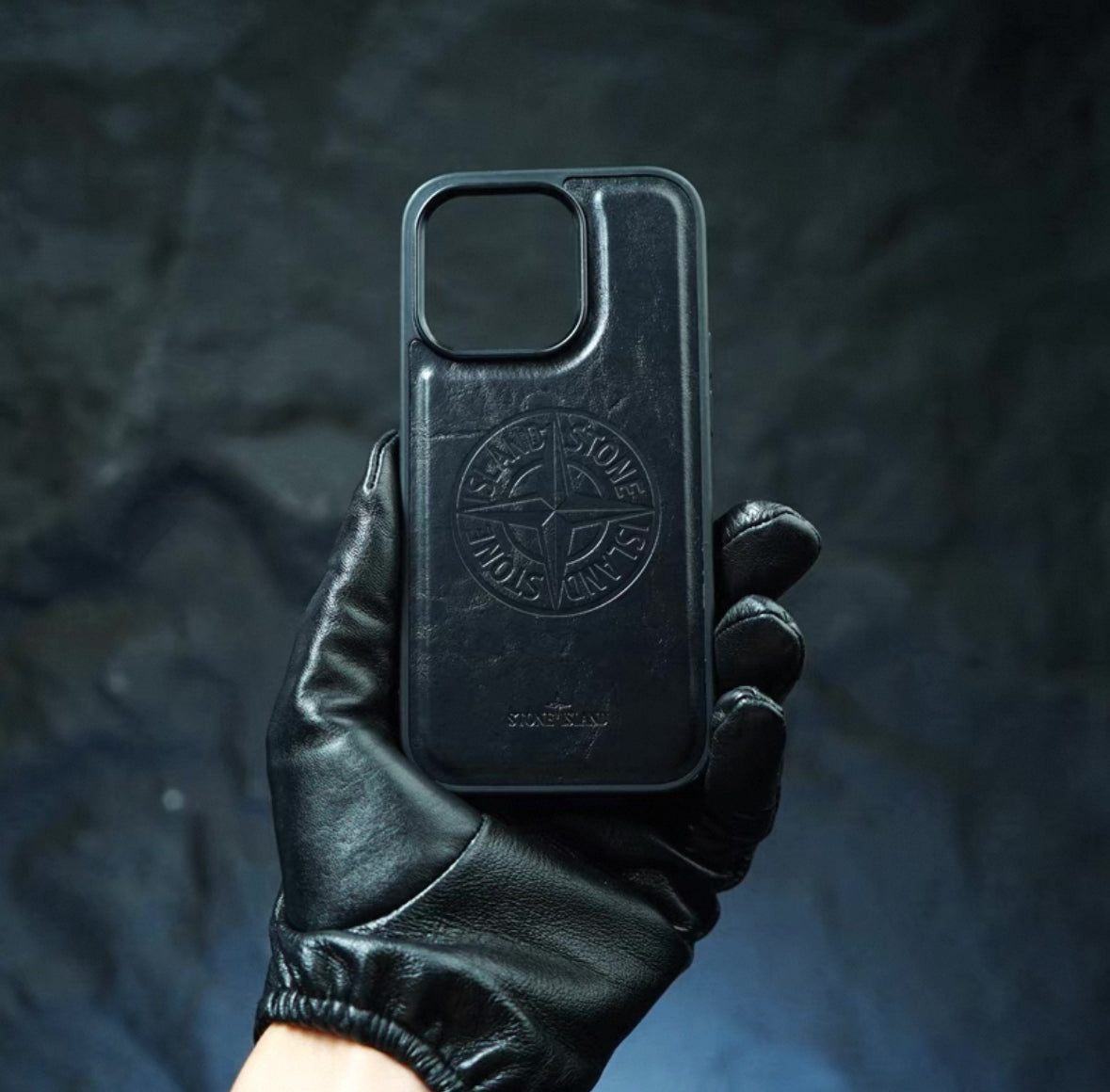 Black Stone Island iPhone case held by gloved hand on dark textured background