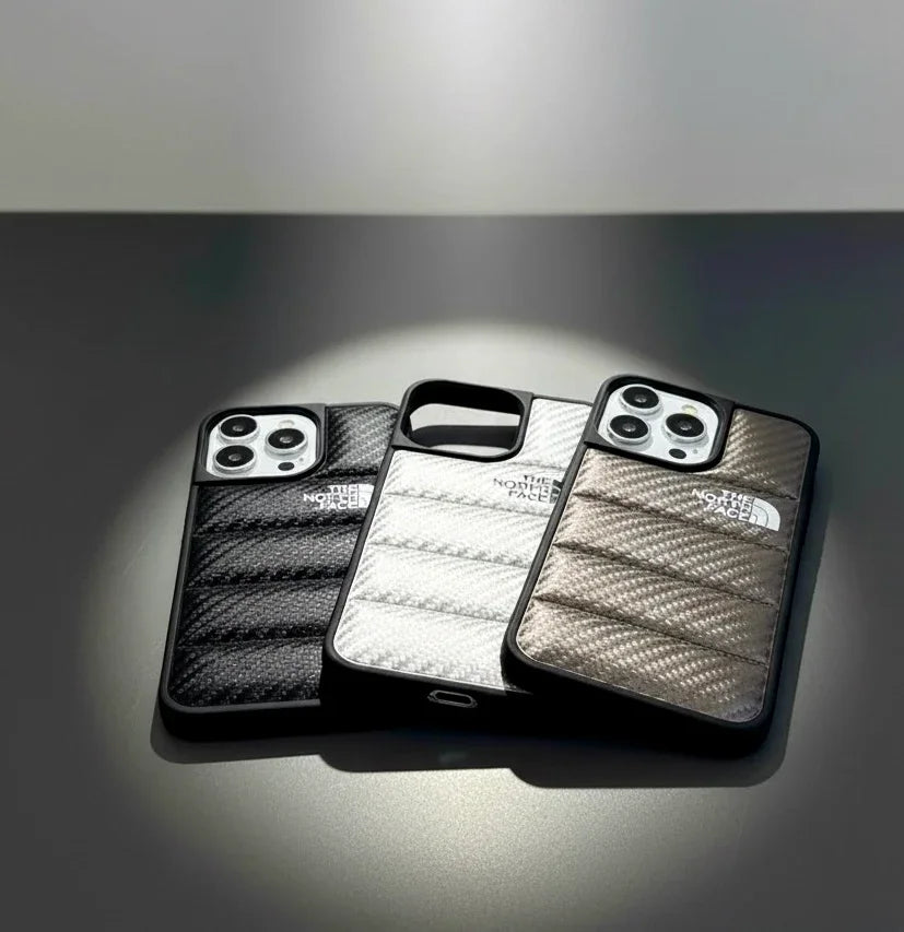 Three The North Face iPhone cases in black, white, and brown on a sleek gray surface