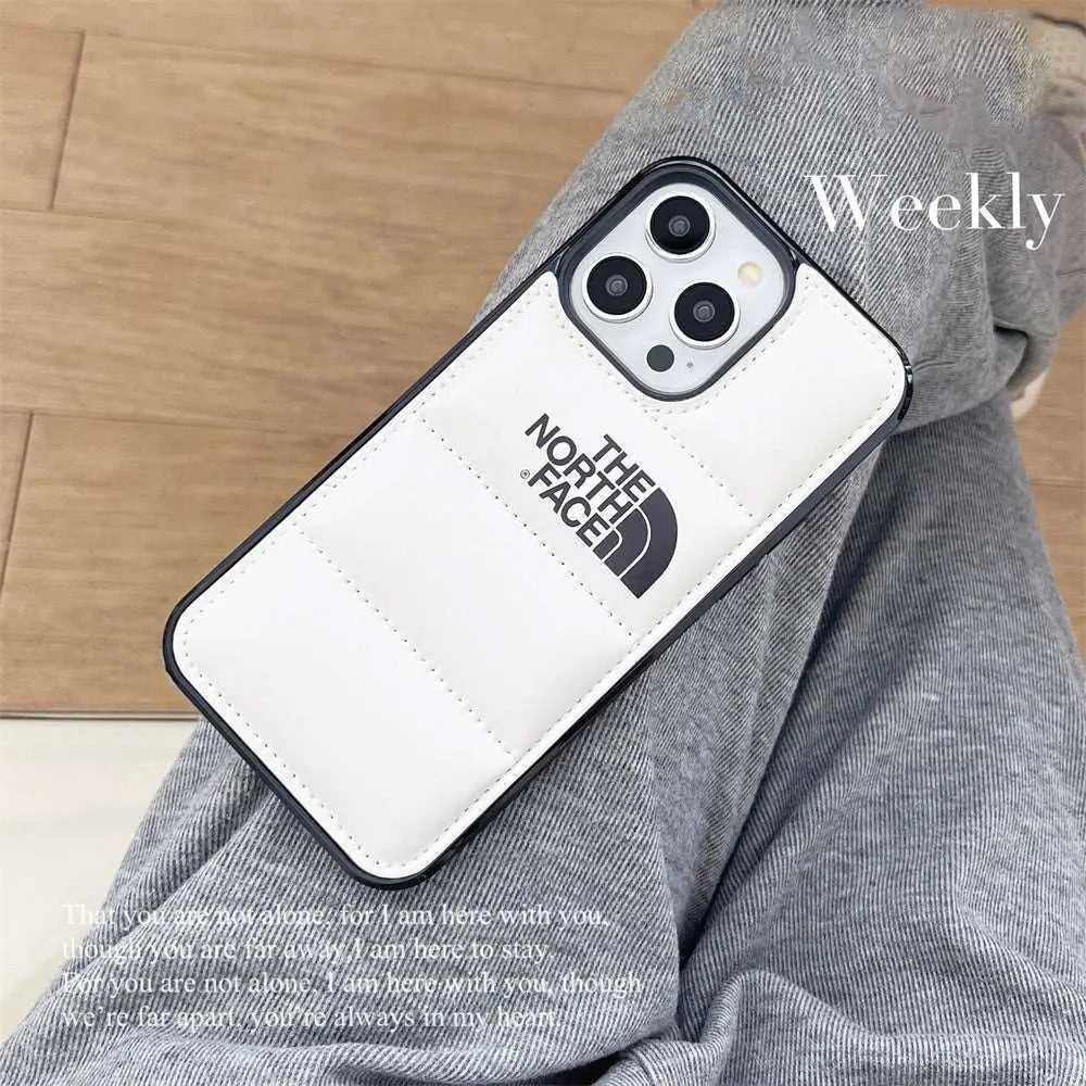 White padded North Face iPhone case on person wearing grey pants, wooden floor background