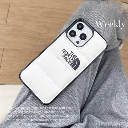 White padded North Face iPhone case on person wearing grey pants, wooden floor background