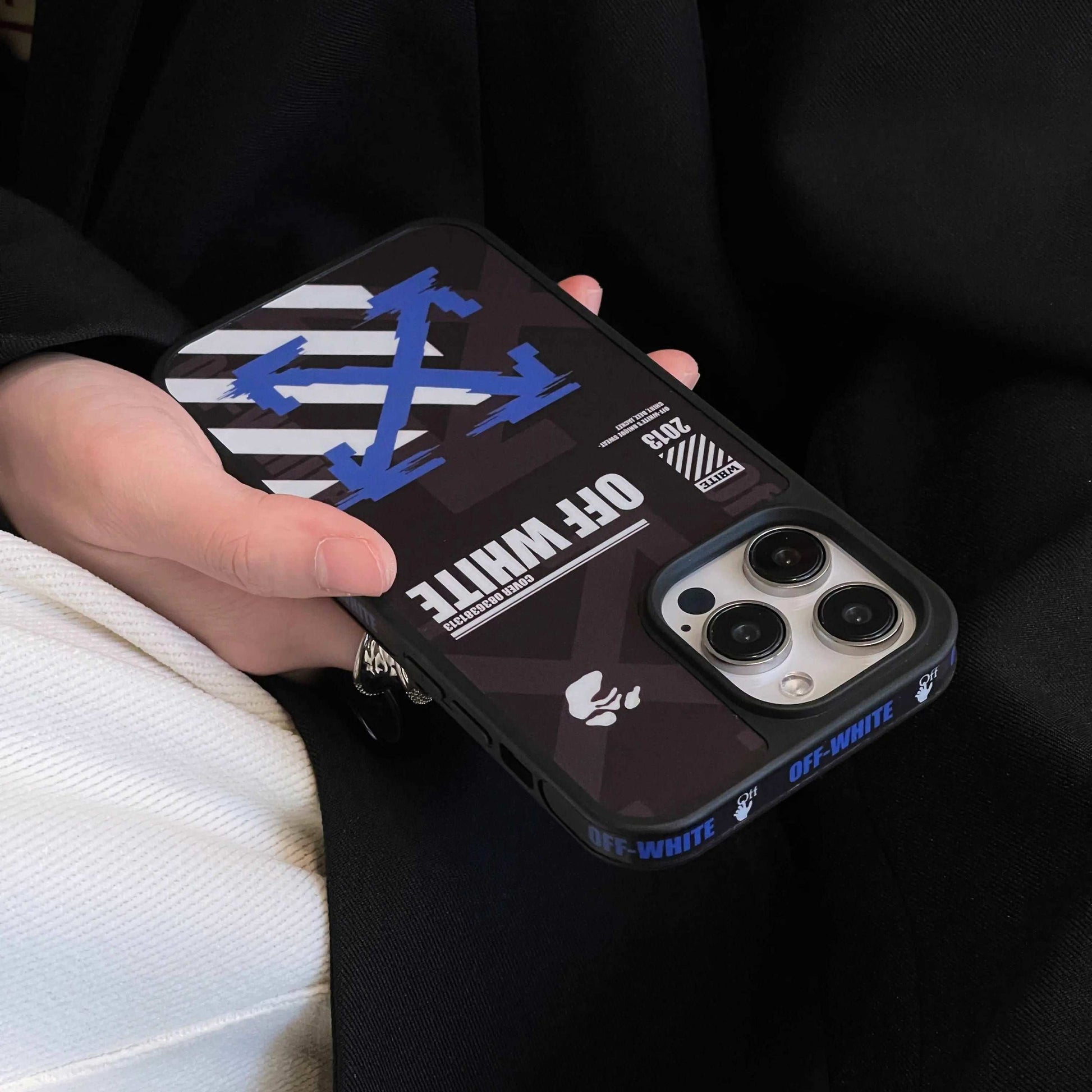 Hand holding iPhone with Off-White logo blue arrow graphic phone case, bold branding visible