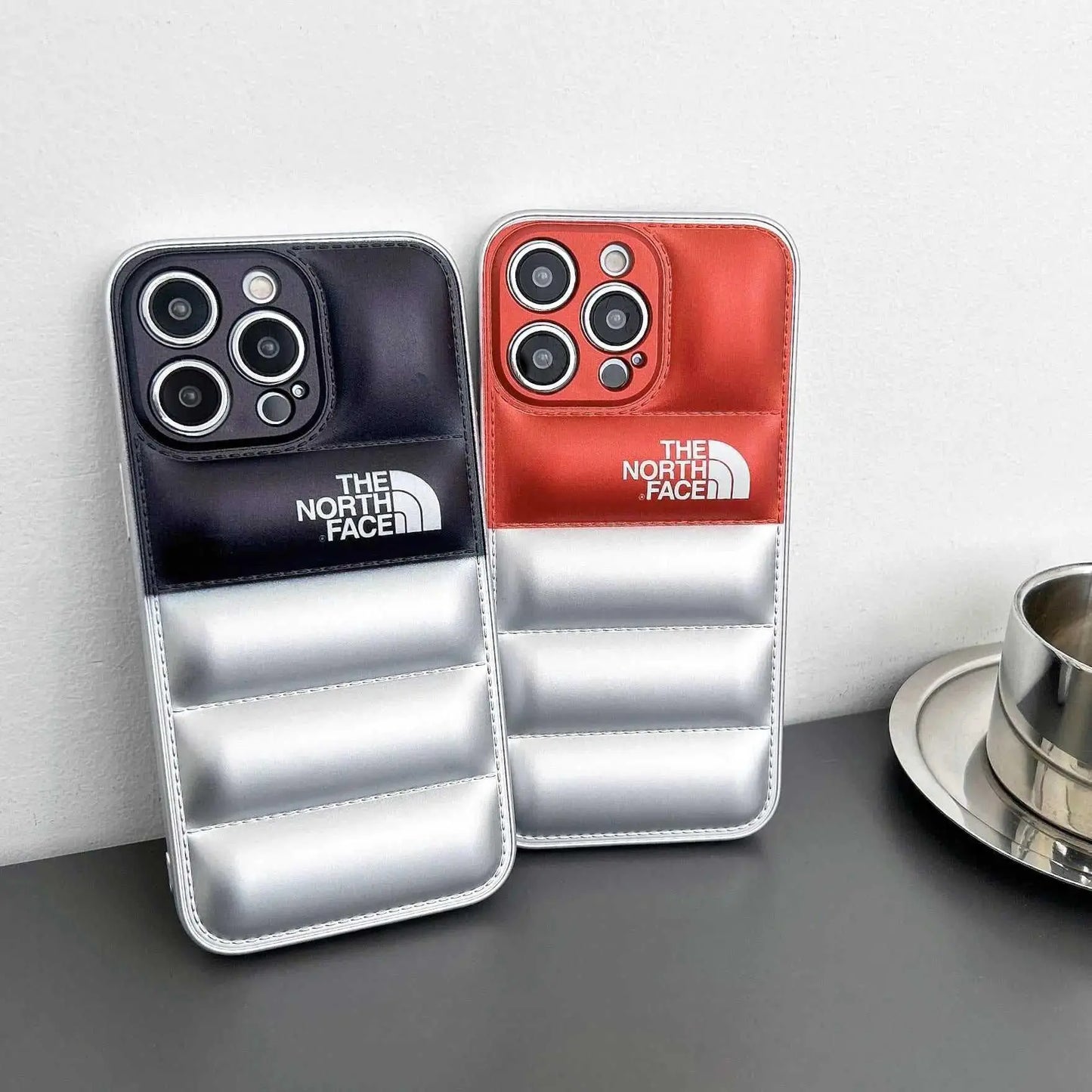 Two puffer-style North Face iPhone cases in black and red on a table