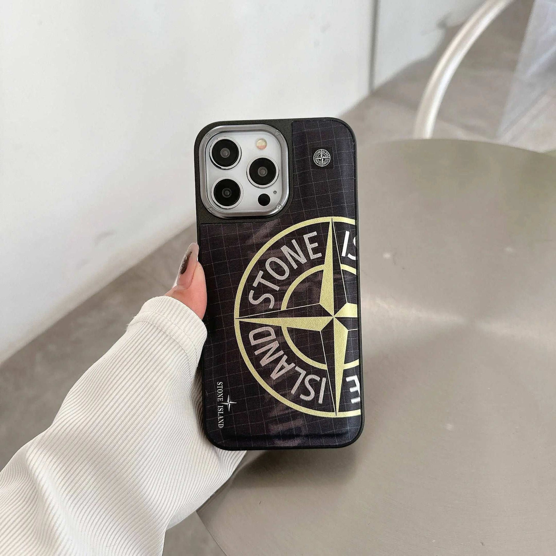 Person holding iPhone with black Stone Island logo case on modern table