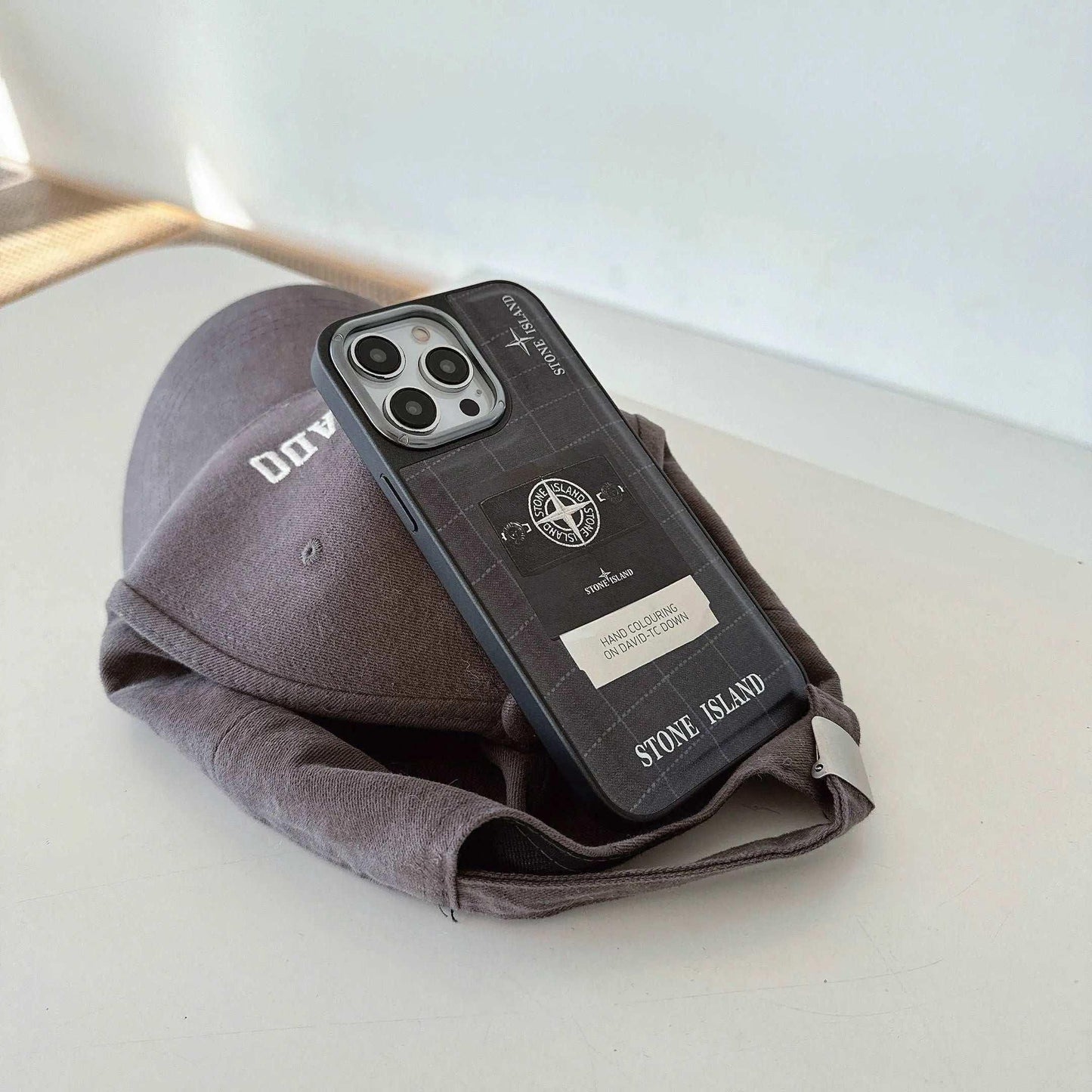 Stone Island iPhone case on gray baseball cap on white surface