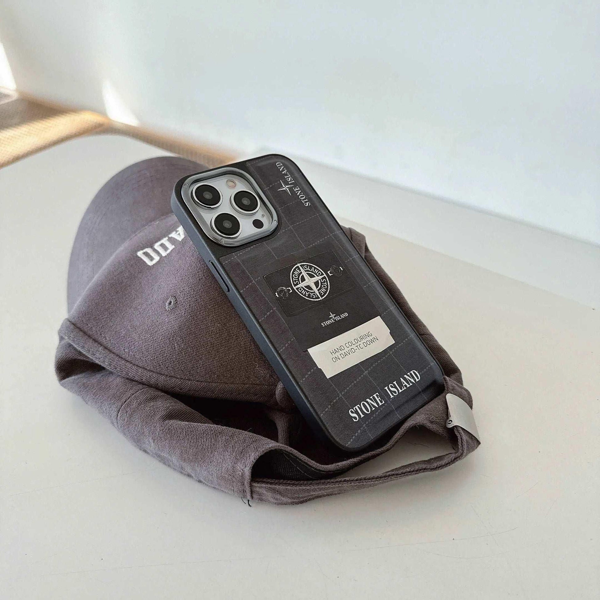 Stone Island iPhone case on gray baseball cap on white surface