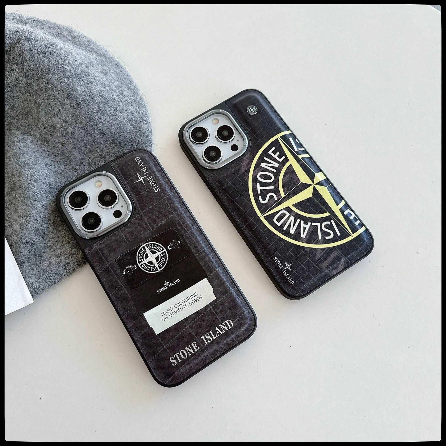 Stone Island branded iPhone cases on white surface with gray fabric background