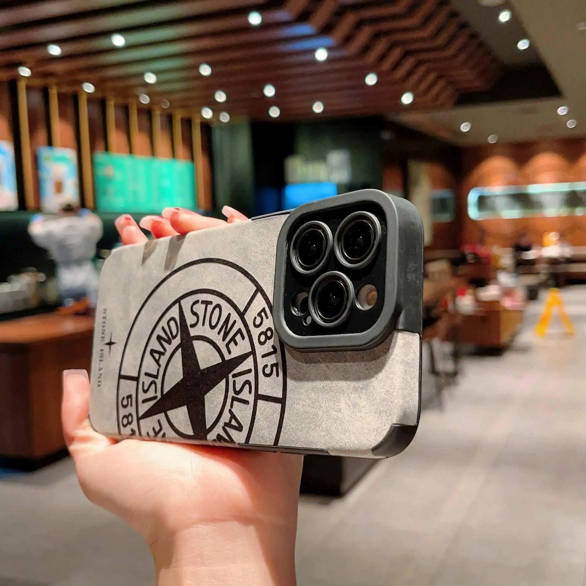 Stone Island iPhone case held in a modern café, showing bold logo design.