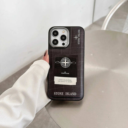 Stone Island iPhone case with logo and patch design held in hand on a gray table.